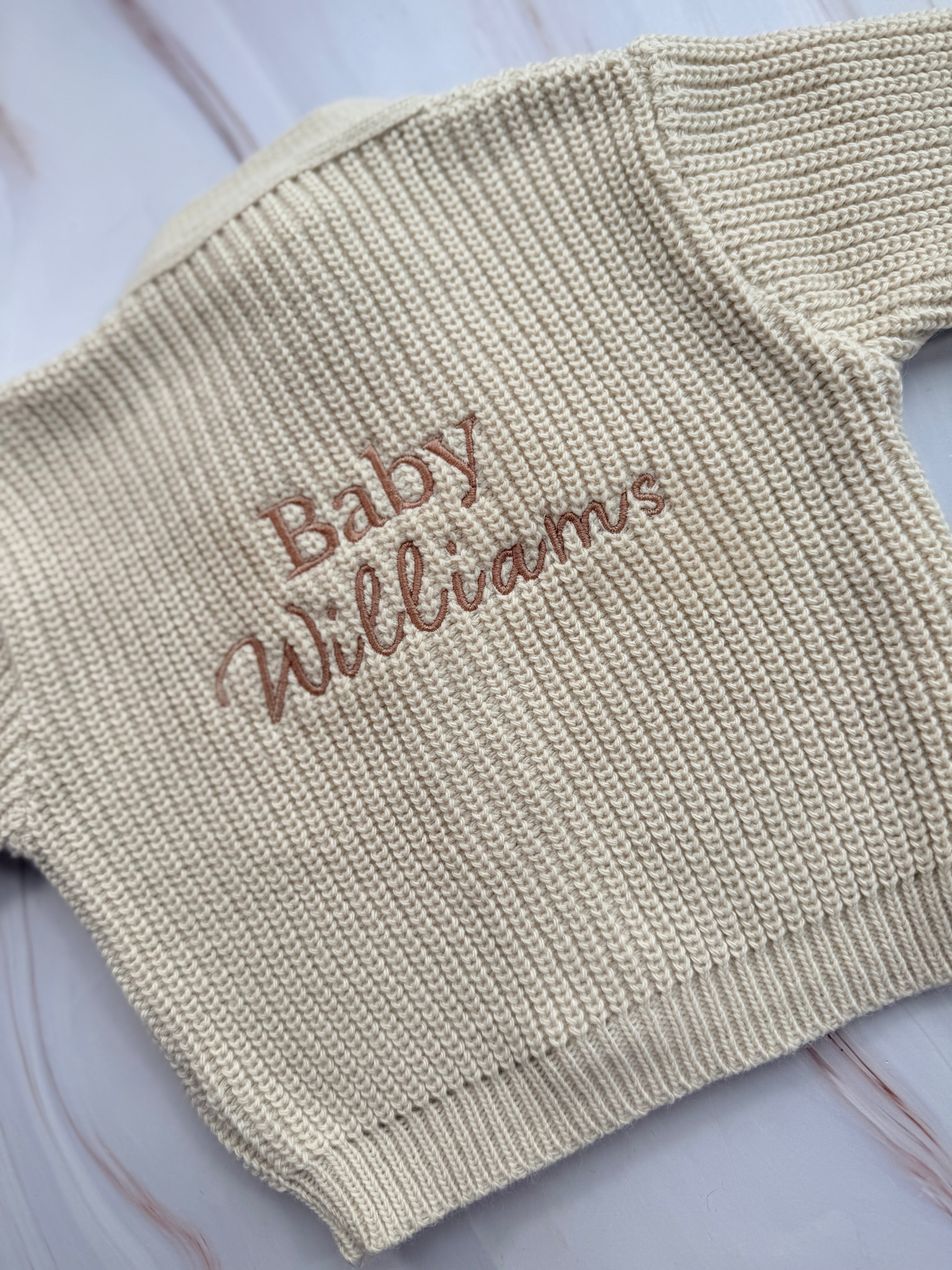 Beige baby sweater with 'Baby Williams' embroidery on a light background